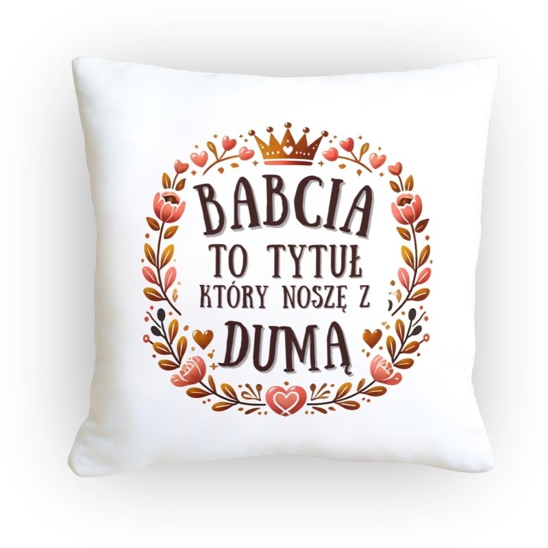 Poduszka z napisem Dumna Babcia ozdobiona kwiatowym motywem i koroną, leżąca na jasnym futrze i drewnianym tle.