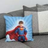 Poduszka z chłopcem jako superbohaterem w czerwonej pelerynie i niebieskim stroju na tle promieni